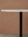 A close-up of the Harbour Column Dining Table with a white marble top and a black column base, set against a terracotta wall.