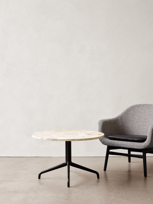 A Harbour Column Lounge Table with a light stone top and black star base, next to a grey upholstered Harbour Lounge Chair.