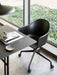 The Harbour Dining Chair, with a black star base and casters, is shown at a black desk next to a window with a garden view.