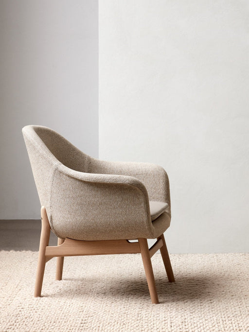 A Harbour Lounge Chair with light beige textured upholstery and a natural oak frame, side view in a minimalist room.