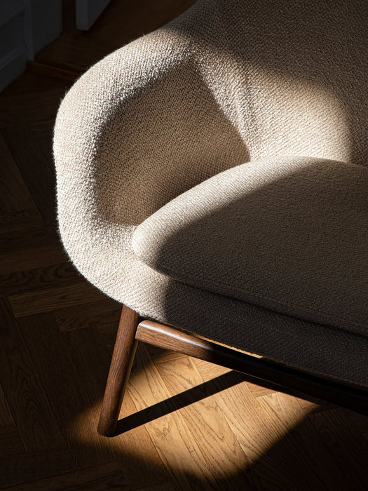 A detailed shot of the Harbour Lounge Chair, highlighting its beige bouclé upholstery and dark wood frame in sunlight.