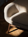 A detailed shot of the Harbour Lounge Chair, highlighting its beige bouclé upholstery and dark wood frame in sunlight.