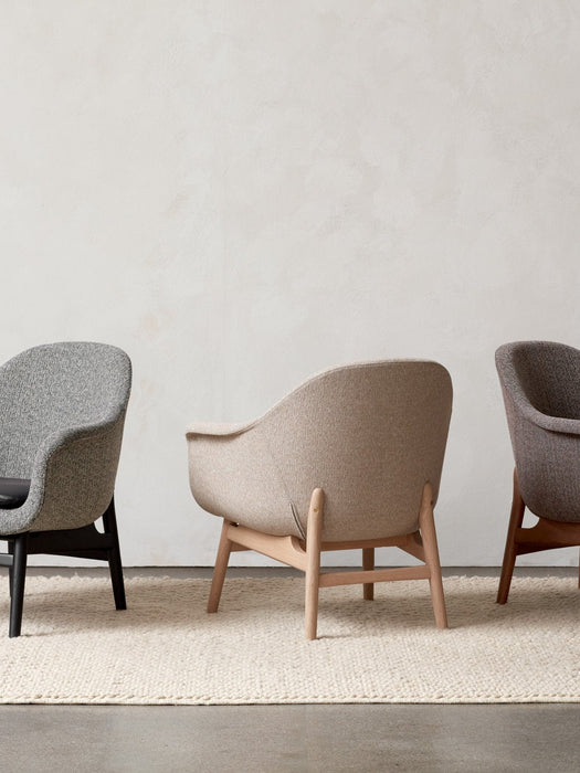 Three Harbour Lounge Chairs with different upholsteries and wood frames are lined up against a plain wall on a textured rug.