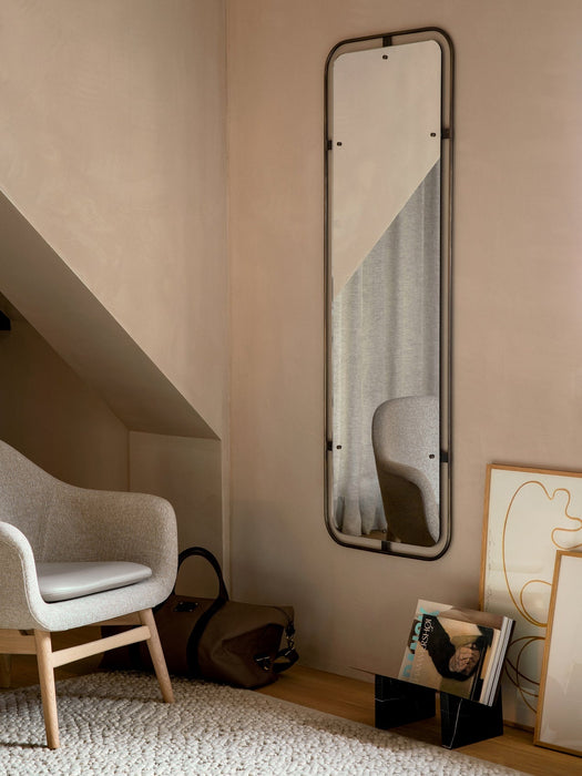 A light grey Harbour Lounge Chair sits on a textured Gravel Rug in a room corner beside a tall Nimbus Mirror and framed art.