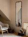 A light grey Harbour Lounge Chair sits on a textured Gravel Rug in a room corner beside a tall Nimbus Mirror and framed art.