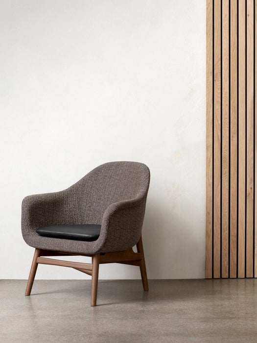A brown fabric Harbour Lounge Chair with a dark wood frame and black cushion, set against a white wall and wood slat panel.