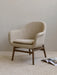 A beige Harbour Lounge Chair with a dark wood frame on a striped rug in a minimalist room, with a magazine on the floor.
