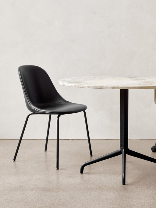 The Harbour Side Dining Chair, upholstered in black with a black steel base, sits beside a round marble dining table.
