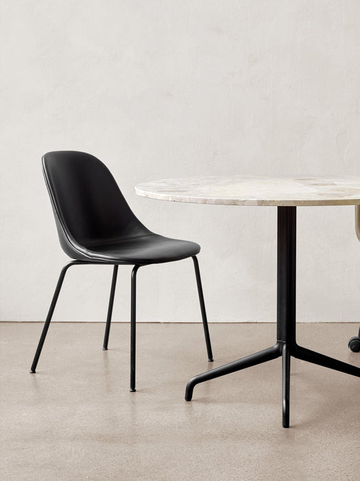 The Harbour Side Dining Chair, upholstered in black with a black steel base, sits beside a round marble dining table.