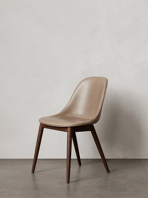 A Harbour Side Dining Chair with a beige leather upholstered shell and dark stained wooden base, against a plain wall.
