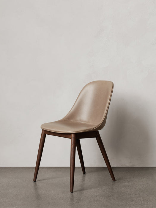 A Harbour Side Dining Chair with a beige leather upholstered shell and dark stained wooden base, against a plain wall.