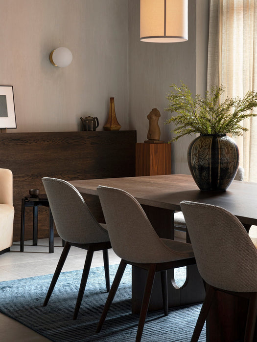 Side view of the Androgyne Dining Table and Harbour Chairs on a blue Houkime Rug, with a Tearoom armchair in the background.