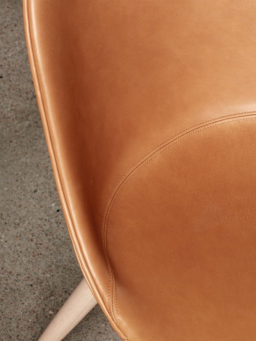 Close-up of the Harbour Side Dining Chair's tan leather seat, highlighting its fine stitching and light oak leg.