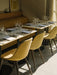 Three yellow upholstered Harbour Side Dining Chairs with wood legs around marble Harbour Column Tables in a restaurant.