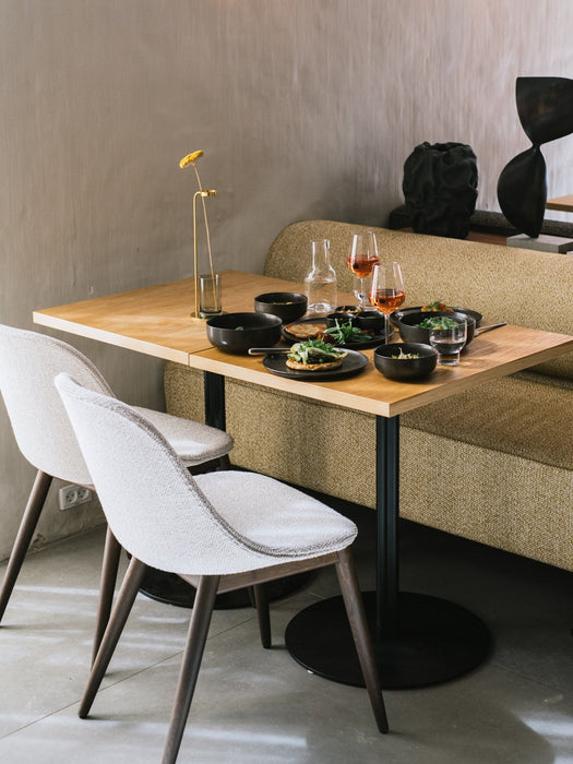 Two light-upholstered Harbour Side Dining Chairs with wooden bases at a dining table set for two, next to a yellow sofa.