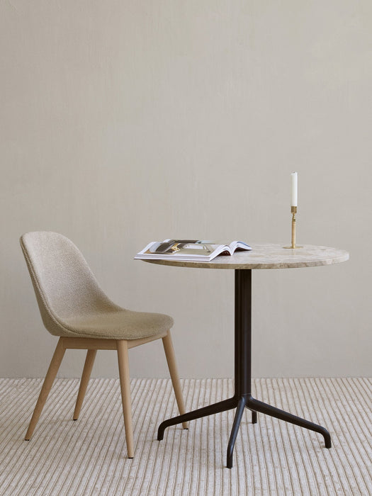 A beige upholstered Harbour Side Dining Chair with wood legs sits beside a marble-top table with a magazine and candlestick.
