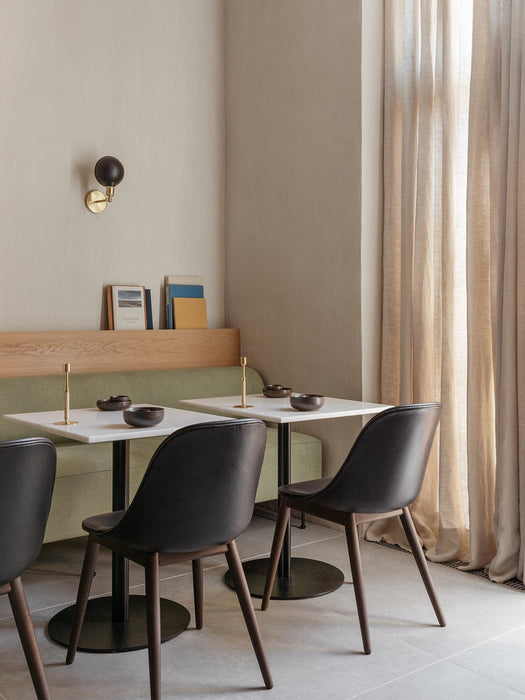A restaurant corner featuring black leather Harbour Side Dining Chairs at white tables next to a green upholstered bench.