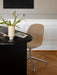 A Harbour Side Dining Chair with brown upholstery and a star base at a black table with a vase on a herringbone floor.
