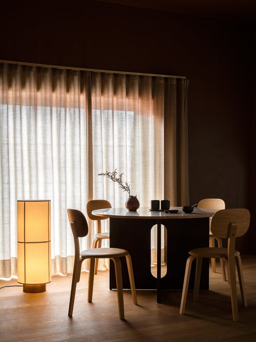 The Hashira Floor Lamp provides a warm glow in a dining room, beside an Androgyne Dining Table and Afteroom Plywood chairs.