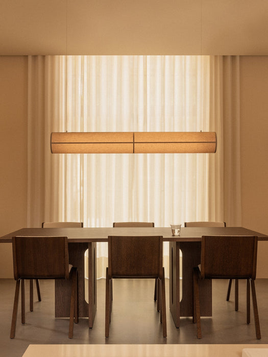 The Hashira Linear Pendant Lamp illuminates an Androgyne Dining Table and Ready Dining Chairs in a serene, warmly lit room.