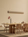 The Hashira Linear Pendant Lamp hangs over an Androgyne Dining Table set with Ready Dining Chairs and a Stance Vase.