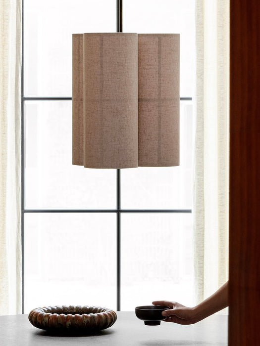 The Hashira Pendant Lamp, Cluster, with three raw linen shades, hangs over a dark table with ceramic bowls by a window.