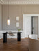 The white Hashira Pendant Lamp hangs over a black desk and chair in a room with beige panelled walls and a herringbone floor.