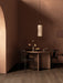 The Hashira Pendant Lamp hangs over a wooden Androgyne Dining Table with Merkur Dining Chairs in a brown-toned room.