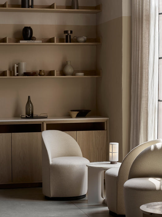 A lit Hashira Table Lamp, Portable, on a side table between two cream Tearoom Side Chairs in a cozy, minimalist room.