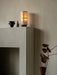 The Hashira Table Lamp, Portable, glows warmly on a grey mantelpiece next to two small vases, against a textured beige wall.