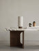 Hashira Portable Table Lamp with a linen shade sits on a marble Androgyne Lounge Table next to a book and decorative items.