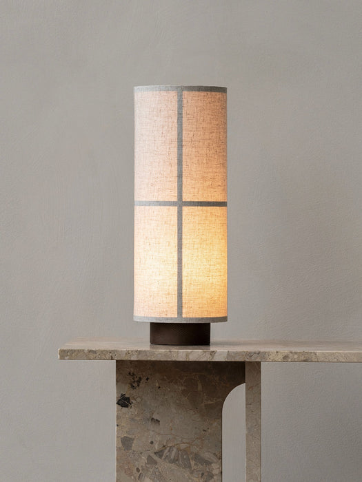 A close-up of the lit Hashira Table Lamp with a raw linen shade, sitting on a heavy marble Androgyne Lounge Table.