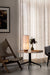 The Hashira Table Lamp emits a warm glow on a marble side table, placed next to a wooden Knitting Chair in a modern interior.