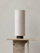 The Hashira Table Lamp, Raw, shown with its cylindrical linen shade and dark wood base, sits on a beige marble console table.
