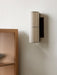 A close-up of the Hashira Wall Lamp in raw linen, mounted on a textured white wall next to a light oak fluted cabinet.