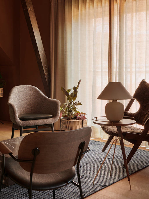 A warmly lit living room showcasing the grey Houkime Rug, surrounded by modern armchairs, a side table, lamp, and plant.