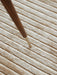 A detailed close-up of the beige Houkime Rug, highlighting its soft, linear texture under the tapered wooden leg of a chair.