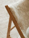 A detailed close-up of a wooden chair frame with a fluffy sheepskin throw, set against the ribbed texture of the Houkime Rug.