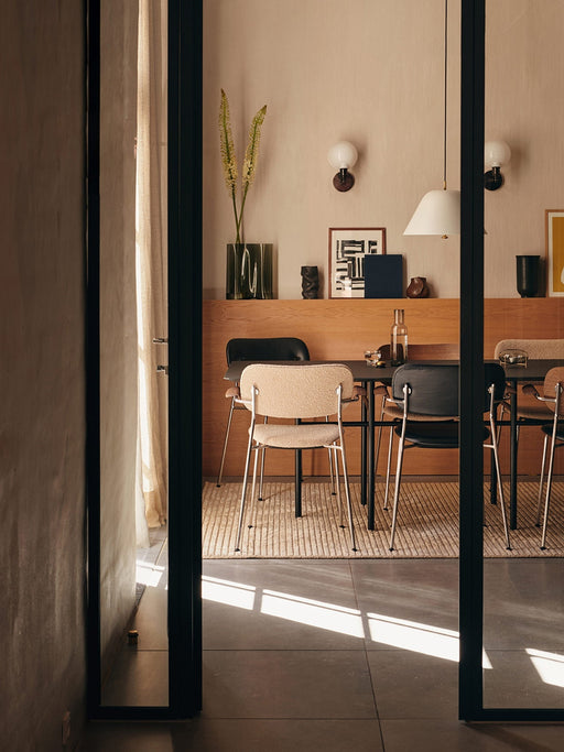 The textured, beige Houkime Rug in a modern dining room setting, placed under a dark dining table with mixed style chairs.