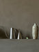 A sleek, brushed steel Hydrous Watering Can and Hydrous Plant Mister next to a rustic ceramic vase on a grey textured shelf.