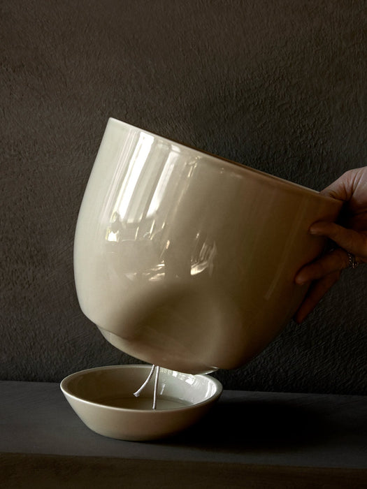 A hand holds the top of the glossy, off-white Hydrous Planter, showing the self-watering wick dangling into the water bowl.