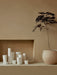 A collection of white Ignus Flameless Candles sits in a beige alcove next to a Plantas Planter holding a small tree.