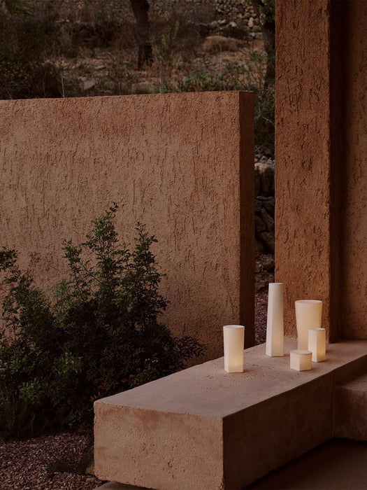 Three cylindrical, bone china Ignus Flameless Candles in various sizes, glowing with a soft, warm light on a neutral surface.