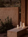 Three cylindrical, bone china Ignus Flameless Candles in various sizes, glowing with a soft, warm light on a neutral surface.