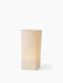 A tall, sculptural Ignus Flameless Candle in off-white, shown at an angle and lit from within with a warm, ambient glow.