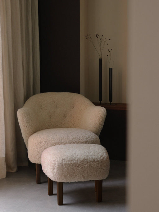 Ingeborg Lounge Chair and ottoman in Moonlight sheepskin, styled in a minimalist room with Stance Vases and a beige curtain.
