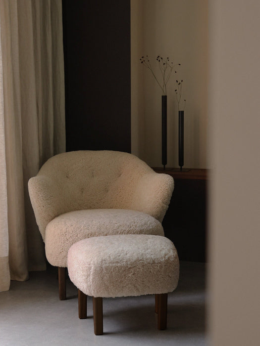Ingeborg Lounge Chair and ottoman in Moonlight sheepskin, styled in a minimalist room with Stance Vases and a beige curtain.