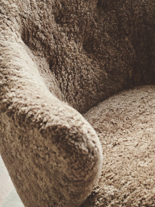 Close-up of the Ingeborg Lounge Chair's armrest and seat, showcasing the plush, curly texture of the brown sheepskin.