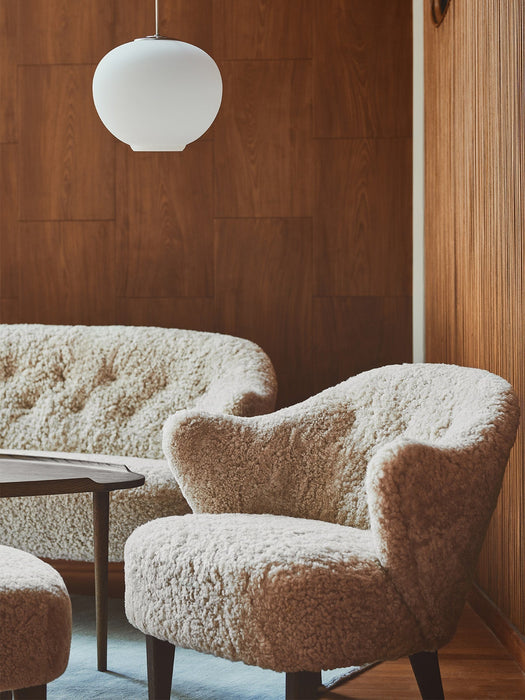 The Ingeborg Lounge Chair and Sofa in off-white sheepskin, styled in a cosy room with dark wood-panelled walls.