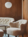 The Ingeborg Lounge Chair and Sofa in off-white sheepskin, styled in a cosy room with dark wood-panelled walls.